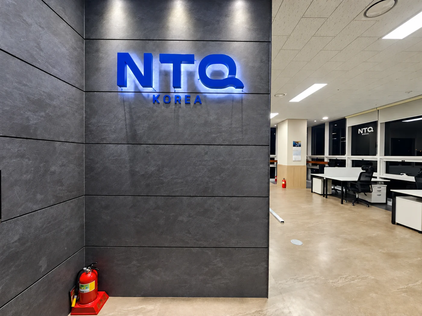 회색 벽면의 파란 NTQ KOREA 사인과 사무실 업무공간